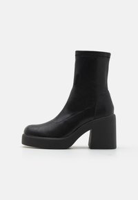 Bottines noires avec une texture en cuir lisse, un bout rond et un large talon bloc. Couture autour de la zone de la cheville.