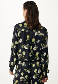 Blusa a maniche lunghe in tessuto nero con stampa di pere verdi e fiori bianchi. Presenta una vestibilità comoda e polsini con bottoni. Texture liscia.