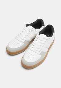 Weiße Sneaker mit einer glatten Lederoberfläche, grauen Akzenten, perforiertem Zehenbereich, weißen Schnürsenkeln und einer Gummisohle. Schwarzes Innenfutter.
