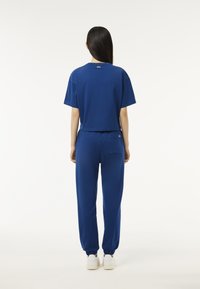Blaues Baumwoll-Cropped-T-Shirt mit kurzen Ärmeln, kombiniert mit passenden Jogginghosen, die elastische Bündchen und eine Gesäßtasche haben. Weiße Schuhe sind sichtbar.