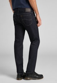 Jeans de mezclilla en un tono azul oscuro con corte recto, con costuras amarillas, bolsillos traseros y una etiqueta de cuero con marca en la cintura.