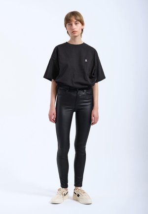 Zwart oversized katoenen t-shirt met een klein logo, gecombineerd met strakke zwarte neplederen broek en crèmekleurige sneakers.