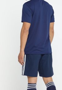 Marinblå atletisk t-shirt med korta ärmar, parat med marinblå shorts med vita sidostråk. Ytterligare randiga blå och vita knästrumpor.