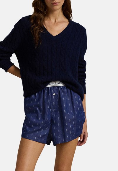 Marineblauwe kabelgebreide trui met een V-hals en lange mouwen, gecombineerd met gestreepte marineblauwe shorts met een logo-band en knoopsluiting.