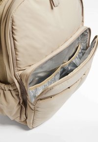Beig ryggsäck med en mjuk, vadderad utsida, en störtlås framtida ficka med silverfärgad isolering och organiseringsfack.