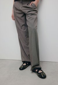 Pantalons taillés gris avec une coupe ample et des plis. Associés à des ballerines noires ornées de clous dorés et d'un trim élastique froncé.