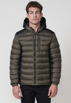 Chaqueta tipo puffer en verde oliva con detalles negros en los hombros, con cierre de cremallera en la parte delantera, capucha y puños acanalados. Material acolchado y texturizado.
