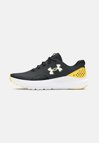 Baskets de sport noires et jaunes avec une tige en mesh, logo blanc distinctif, col rembourré et semelle blanche texturée avec des accents jaunes.