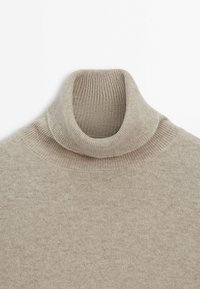 Pull à col roulé en tricot beige avec col en côtes et coutures aux épaules, présenté à plat sur un fond blanc.