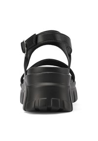 Sandali in pelle nera con cinturino alla caviglia regolabile, suola in gomma spessa e tacco testurizzato. Caratterizzati da un design minimalista e una finitura liscia.