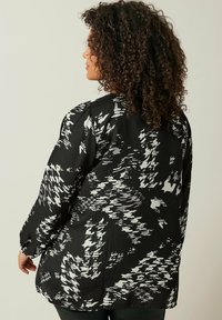Blusa a maniche lunghe con motivo in bianco e nero, tessuto leggero, vestibilità leggermente rilassata e orlo arrotondato. Visualizzazione dal retro.