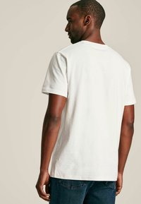 Valge puuvillane T-särk lühikeste varrukatega, ümmarguse kaelusega, millel on sile tekstuur ja mugav lõige. Nähtavad õmblused õlgadel ja külgedel.