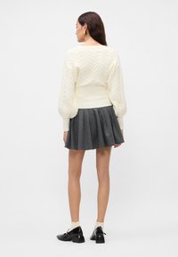 Pullover crem cu tricotaj împletit, cu mâneci bufante, asortat cu o fustă plisată gri cu dungă. Pantofi negri cu toc pătrat și șosete albe până la glezne.