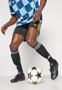 Sorte fodboldstøvler, sorte knæstrømper med grå striber, en blå og hvid mønstret trøje, sorte shorts og en fodbold med stjernedesign.