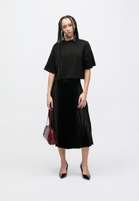 Μαύρο κοντομάνικο μπλούζα, μαύρη πλισέ μίντι φούστα, μαύρες ψηλοτάκουνες γόβες και μπορντό τσάντα χειρός. Απαλή υφή με άνετη εφαρμογή.