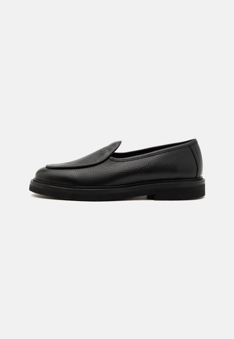Black leather slip-on shoe with a smooth surface, rounded toe, and flat rubber sole. Features a subtle stitched border and minimalist design.