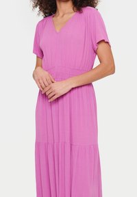 Růžové šaty s krátkým rukávem a výstřihem do V, s nařaseným pasem a volnou skládací sukni. Vyrobeny z lehkého materiálu s hladkou texturou.
