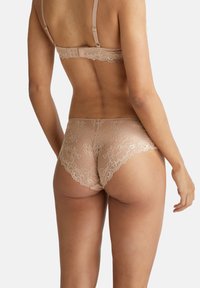 Intimo in pizzo nudo con motivi floreali, bordi ondulati e un design a vita media. Il tessuto è morbido e ha una qualità trasparente.