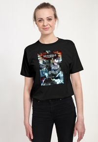 Mladá žena nosí černé tričko s grafikou Death Note, na kterém je postava Ryuka s úsměvem na tváři.