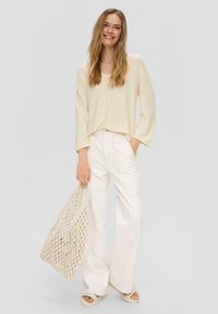 Hellbeige Langarmshirt, weite creamfarbene Hose und eine gestrickte Tragetasche. Strukturierter Stoff mit lockerer Passform und minimalistischem Design.