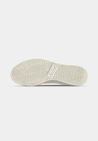 Hvit sneakersåle med teksturert zigzag-mønster, og en sentral logoområde. Materialet ser gummiaktig ut, designet for grep og holdbarhet.