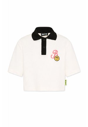 Polo blanc à manches courtes avec col et patte noir, "B" rose texturé et écusson visage triste jaune sur la poitrine gauche.
