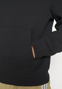 Svart hoodie tillverkad av en blandning av bomull, med en framficka i kängurustil och ribbade muddar. Slät yta med minimala sömnadsdetaljer.