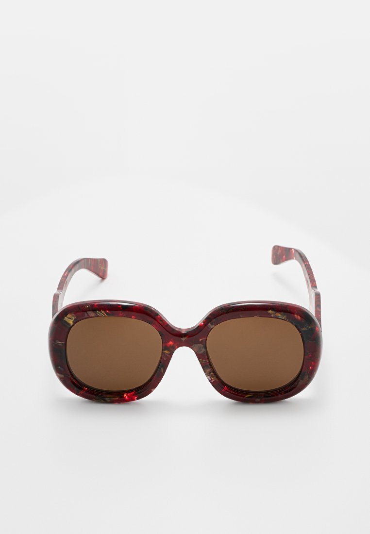 Rote Schildpatt-Sonnenbrille mit übergroßen braunen Gläsern und dicken Rahmen. Die Scharniere sind transparent und haben ein marmoriertes Muster.