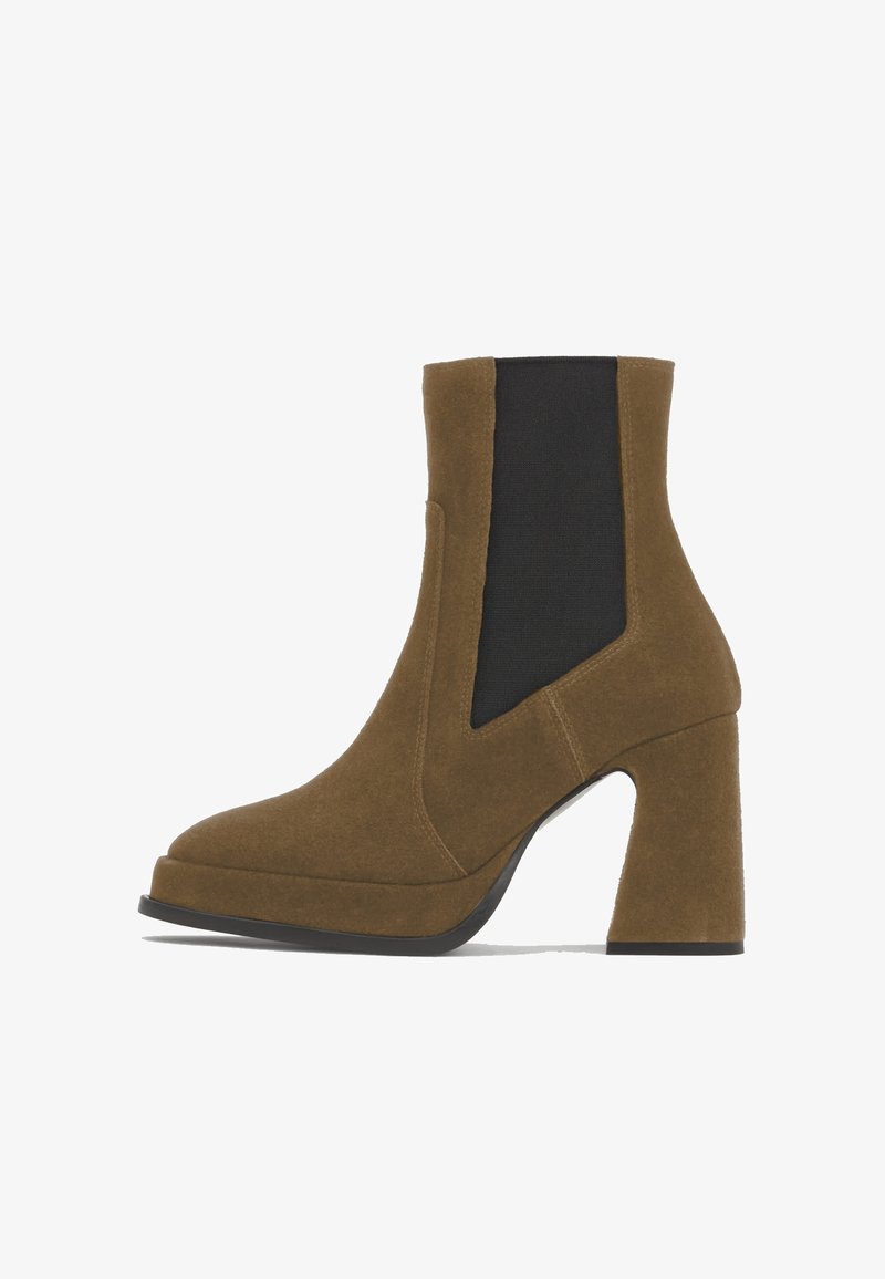 Bottine marron en daim avec talon haut épais, panneau latéral élastique noir et bout arrondi sur fond blanc.