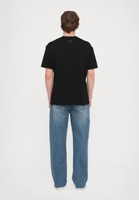 Black cotton t-shirt with a crew neck, featuring a small logo at the back, paired with light blue wide-leg jeans.