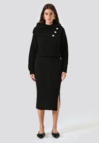 Completo in maglia nera composto da un maglione cropped a coste con colletto ripiegato e tre bottoni decorativi, abbinato a una lunga gonna con design a treccia.