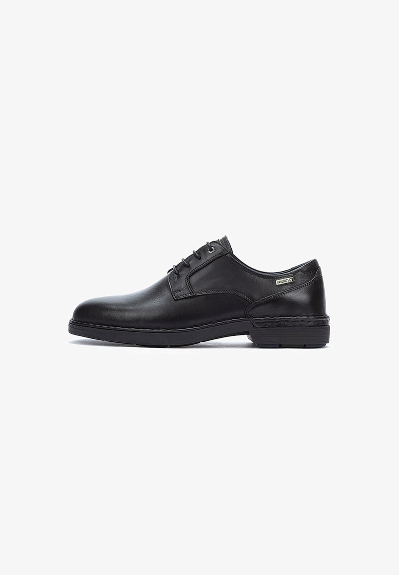 Chaussure habillée pour homme en cuir noir à lacets avec un talon bas et une étiquette en métal de marque sur le côté, présentée en vue latérale gauche sur fond blanc.