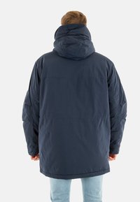 Giacca puffer blu navy con un ampio cappuccio, texture trapuntata e spalle scese. Presenta una linea dritta e polsini elastici.