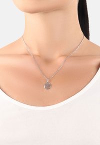 Söljd hängehalsband med en träddesign som hänger från en delikat kedja. Visas mot en vit topp och neutral bakgrund.