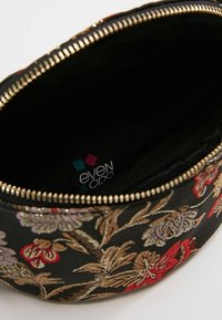 Černý látkový sáček se zlatým zipem, zdobený barevnými vyšitými květinovými vzory v červené, fialové a zlaté barvě. Uvnitř je černá podšívka.