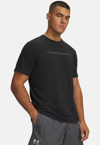 Schwarzes Sport-T-Shirt mit kurzen Ärmeln, Rundhalsausschnitt und dezentem Logodesign auf der Brust. Weicher, glatter Stoff, körperbetonte Passform.