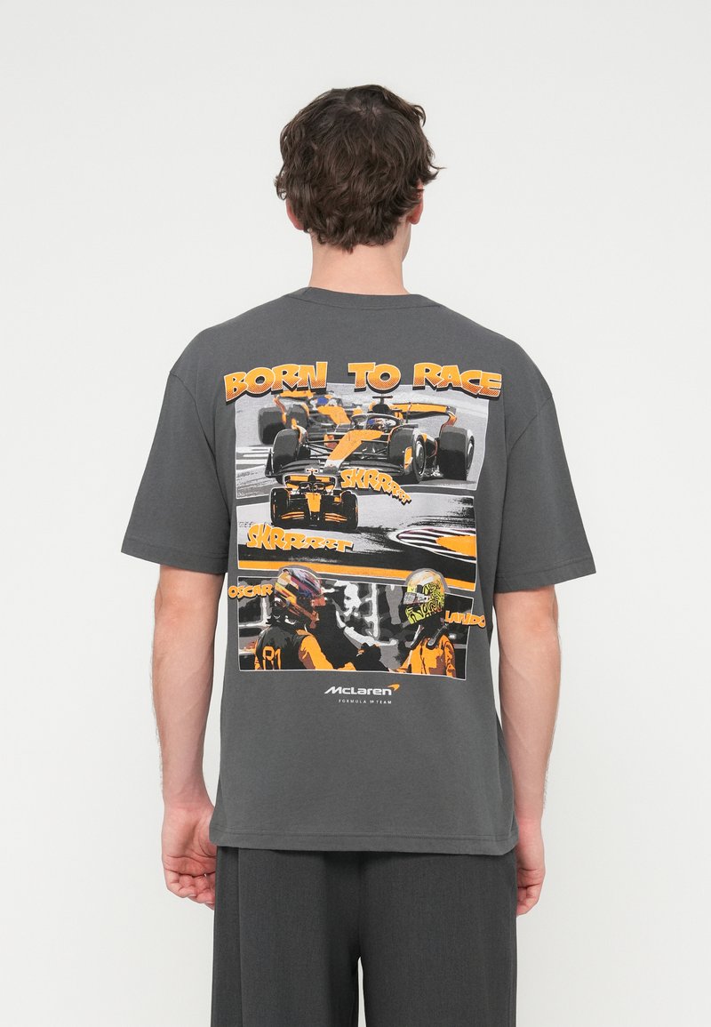 Γκρι βαμβακερό μπλουζάκι με μεγάλο γραφικό τύπωμα που απεικονίζει αυτοκίνητα και οδηγούς της Formula 1. Κείμενο "BORN TO RACE" τονισμένο με πορτοκαλί χρώμα. Κοντά μανίκια.