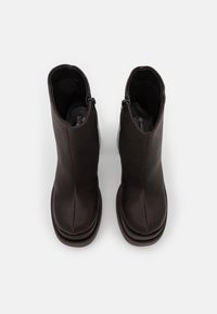 Pareja de botas de cuero negro hasta el tobillo con cremalleras laterales y punteras redondeadas en forma de cuadrado, vistas desde arriba sobre un fondo blanco.