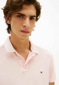 Polo rosa chiaro con colletto classico, caratterizzata da un piccolo logo ricamato sul petto e dettagli di cuciture visibili.