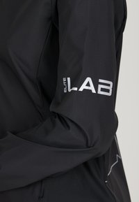 Schwarze Jacke mit strukturiertem Oberflächen, mit einem silbernen "ELITE LAB"-Logo am Ärmel. Elegantes Design mit tailliertem Schnitt.