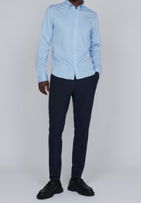 Jasnoniebieska koszula z kołnierzykiem, w połączeniu z ciemnogranatowymi spodniami slim-fit i czarnym obuwiem, na jednolitym tle.