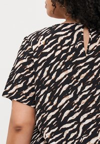 Haut noir avec un motif texturé en vagues blanches et marron clair. Présente un détail en forme de clé à l'arrière et des manches courtes.