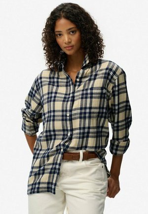 Flanellen shirt in beige en marineblauwe ruit, met een knoopsluiting, lange opgerolde mouwen en een borstzak. Draagt over witte broek.