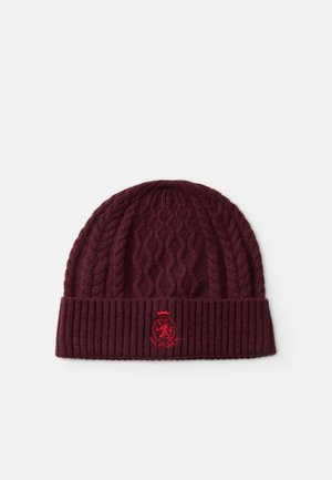 Bordeaux kabelgebreide muts met omgeslagen geribde boord met een rood geborduurd wapen en het woord "HILFIGER" op een witte achtergrond.