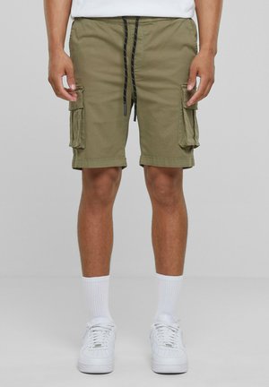 Olivgrüne Cargo-Shorts mit zwei Seitentaschen, schwarzem Kordelzugbund und entspanntem Schnitt. Getragen mit weißen Sneakers und Socken.