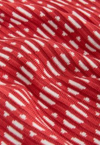 Tissu tricoté rouge avec un motif texturé de rayures horizontales blanches et de points, montrant des plis et des détails de matériau doux.