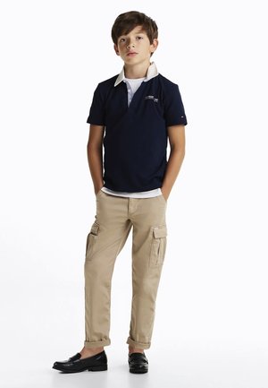 Polo shirt blu navy con colletto bianco a contrasto, pantaloni cargo beige con tasche laterali e mocassini neri. Design di outfit semplice e casual.