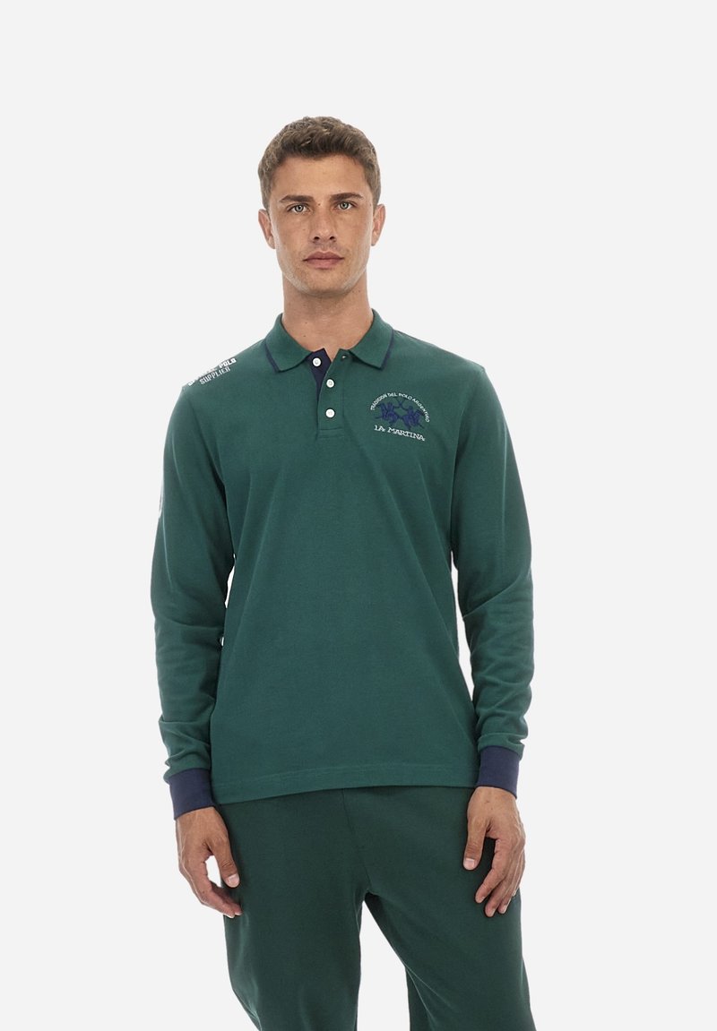 Zelena dolgi rokav polo majica, ki ima mornarsko modro ovratnik, vezenine in sproščen kroj. Material izgleda mehak in teksturiran.