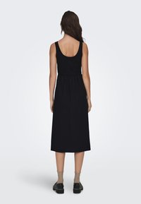 Mustapuku maxi, jossa on ribattu yläosa, ympyräselkä ja joustava vyötärö. Yhdistetty mustiin kenkiin ja läpinäkyviin, frillatehtyihin nilkkasukkasiin.