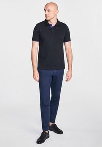 Czarna koszulka polo z fioletowymi akcentami, w zestawie z granatowymi spodniami i czarnymi trampkami, z klasycznym kołnierzykiem i zapięciem na dwa guziki.